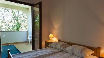 A bedroom with a bed, a nightstand, a lamp, and a view of the outside.