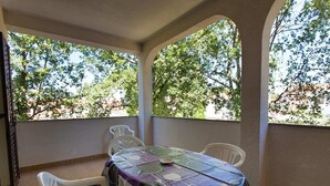 A covered outdoor dining area with a table and chairs, large windows with a view of trees, and a blue carpet.