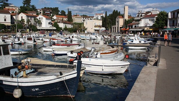 A marina with multiple boats docked, surrounded by buildings and a clear sky.