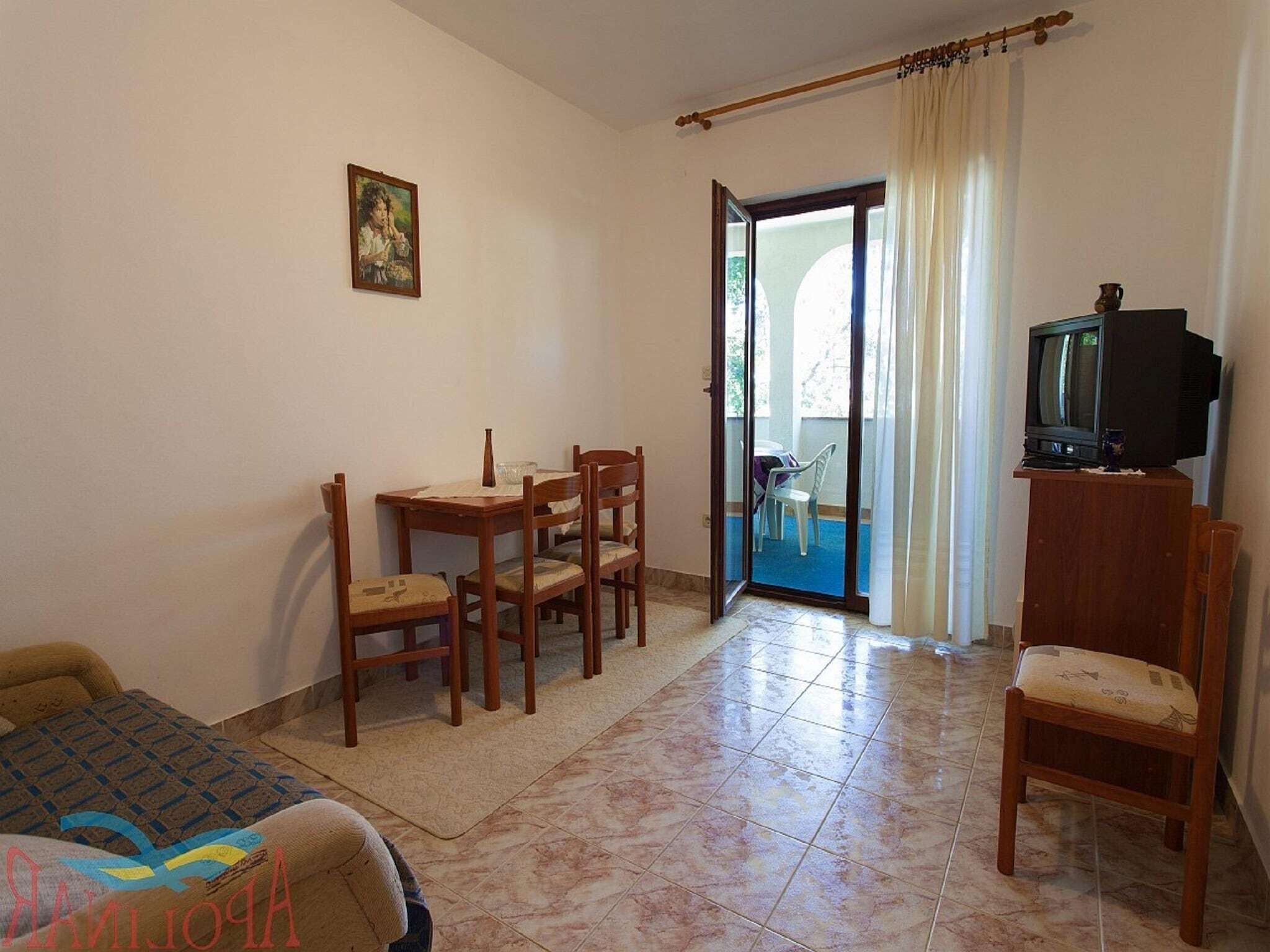 Una habitación con cama, una mesa con sillas, un televisor sobre un mueble bajo y un balcón con vistas.
