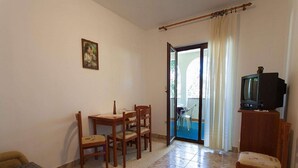 A room with a bed, a table with chairs, a television on a stand, and a balcony with a view.