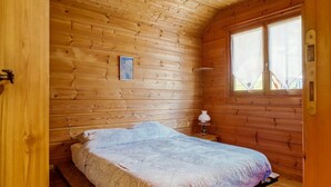 Une chambre dans une cabane en bois, avec un lit, une fenêtre et une petite table sur laquelle se trouve une lampe.