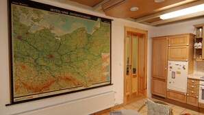 Une pièce avec une grande carte accrochée au mur, des meubles en bois, un radiateur et une table sur laquelle se trouvent un livre et une télécommande.