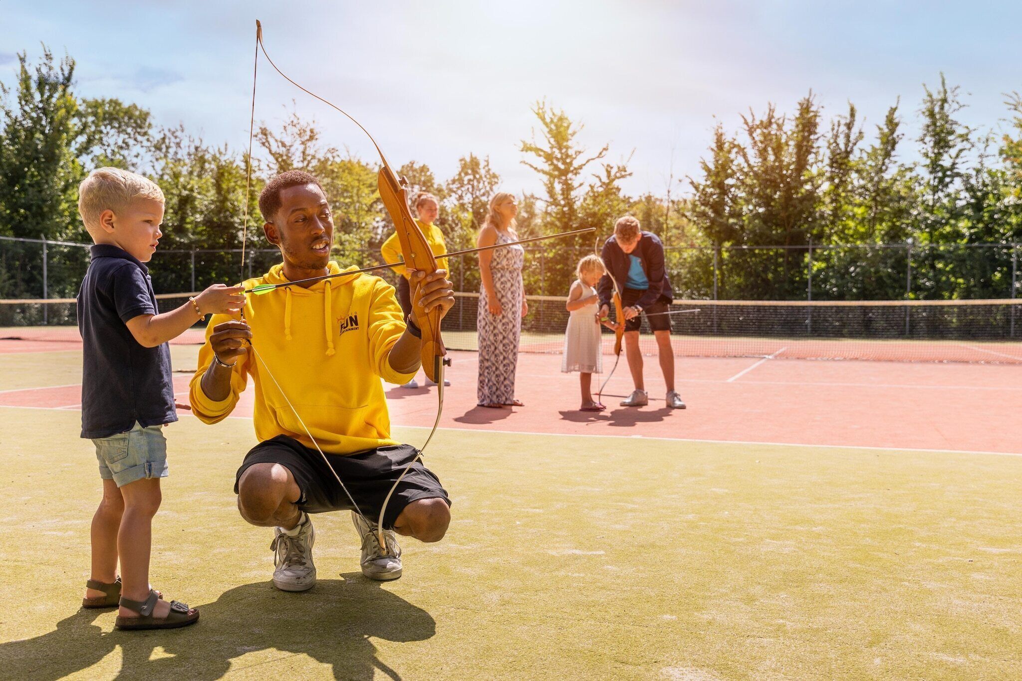 A group of people on an outdoor sports court with a netted fence and trees in the background.