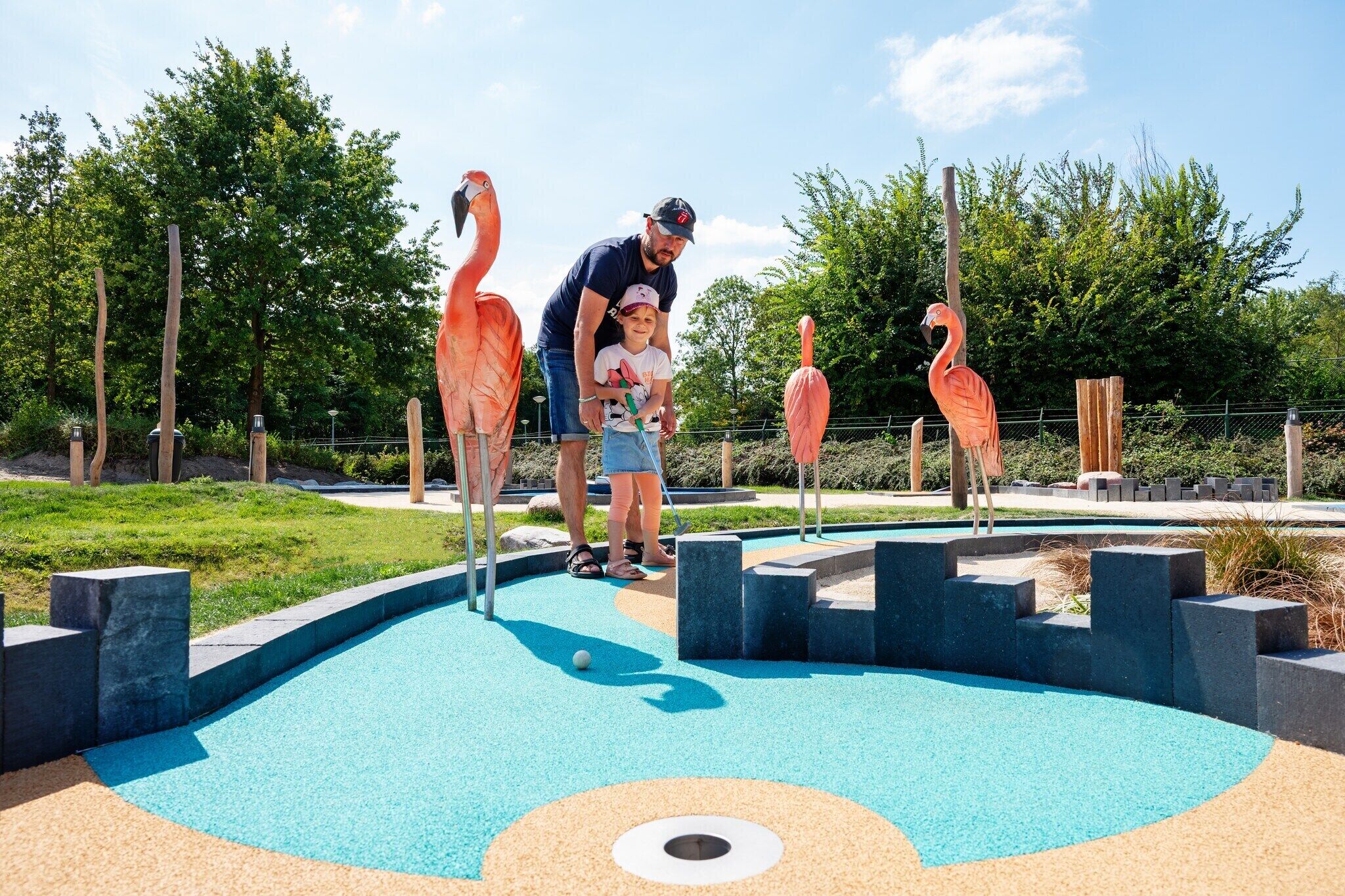 A miniature golf course with flamingo-themed obstacles and a blue playing surface.