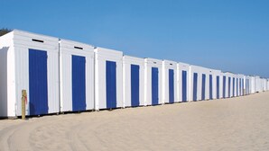 A row of white portable cabins with blue doors on a sandy beach.