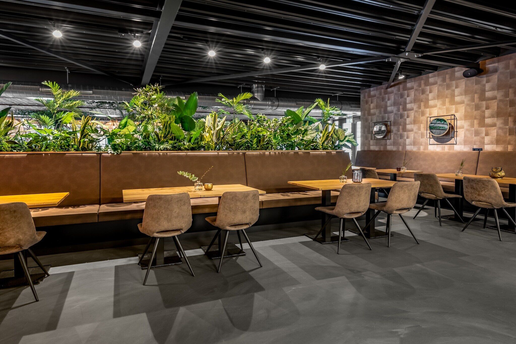 Een modern restaurantinterieur met houten tafels en stoelen, een wand vol planten en een geruit ontwerp aan de muur.