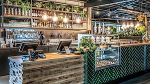 Uma área de bar com balcão de madeira, diversas torneiras e prateleiras repletas de garrafas e copos.