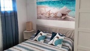 Et soveværelse med seng, sengetøj med striber og vægkunst med maritimt tema.