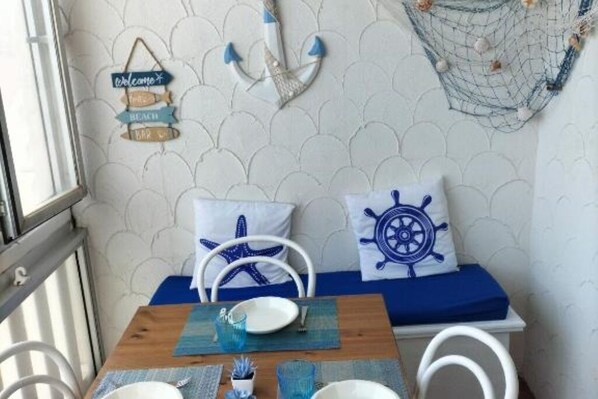 A room with a wooden table, two white chairs, a blue bedspread, and nautical-themed decor including a starfish pillow and a ship's wheel pillow.