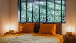 A bedroom with a bed, two bedside tables with lamps, and a window with blinds.
