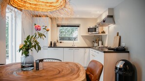 A modern kitchen with white cabinets, a microwave, and a stove. There is a window with a view of trees, and a vase with flowers on the table.