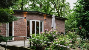 A brick building with a sign reading "Weilpaalthe." It has a covered entrance with a white umbrella and a small garden area with flowers and shrubs.