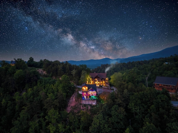 A house with a starry night sky, surrounded by dense forest.