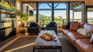 A cozy living room with a fireplace, a wooden coffee table with snacks, leather sofas, and large windows offering a scenic view. - Incredible Sunset Views | Organic Decor | Arcades (Sevierville)