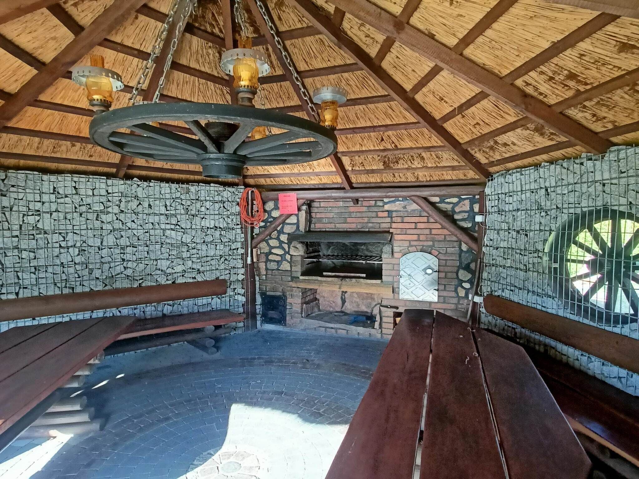 Un interior rústico de madera con pared de piedra, un horno de ladrillo y bancos de madera.