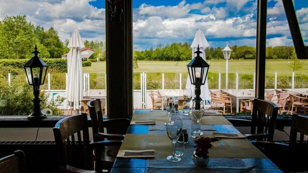 An outdoor dining area with tables set for two, chairs, and a view of a golf course.