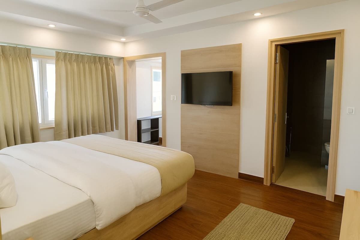 A modern hotel room with a large bed, a flat-screen TV mounted on the wall, and a wooden door leading to a bathroom.