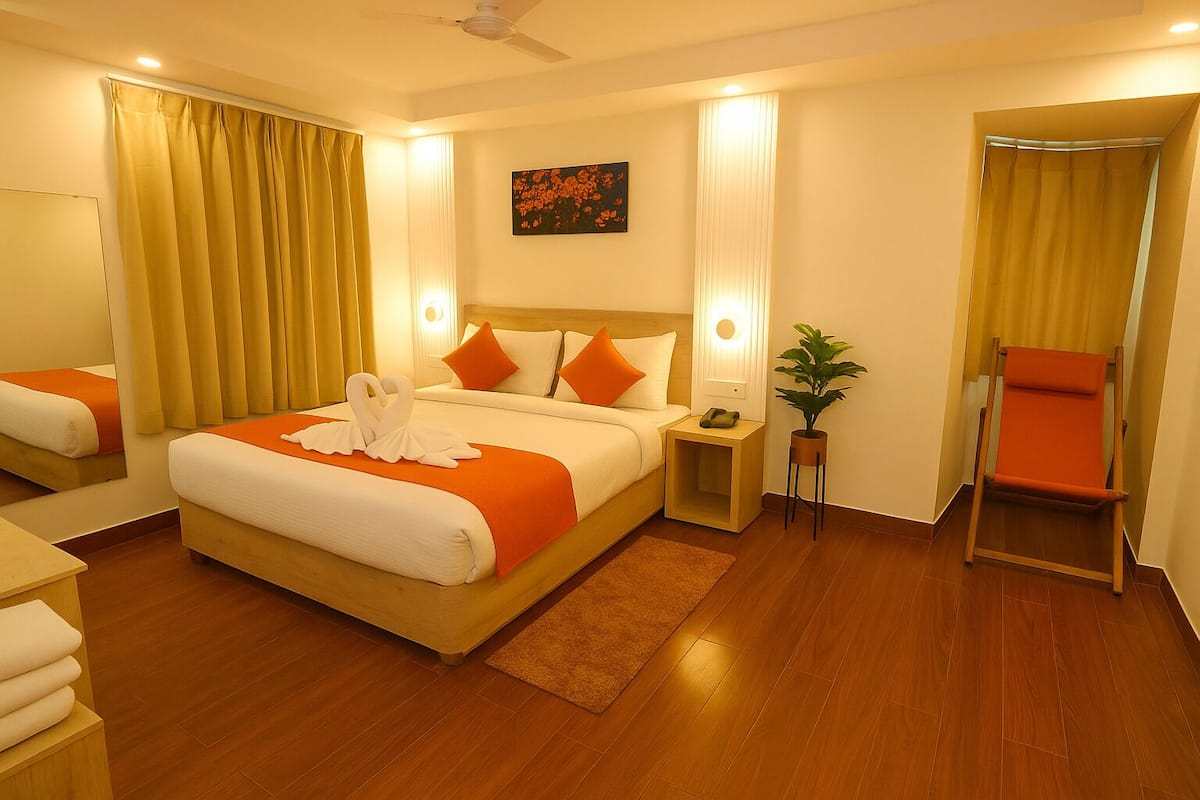 A hotel room with a large bed, a bedside table, a chair, a plant, and a painting on the wall.