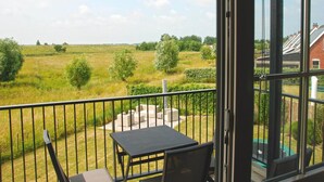 A balcony with a table and chairs, overlooking a grassy field and a residential area. - Apartment in Colijnsplaat near Lake and Sauna (Colijnsplaat)