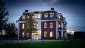 A large, two-story house with a brick exterior and multiple windows, surrounded by a well-maintained lawn. - Apartment in Colijnsplaat near Lake and Sauna (Colijnsplaat)