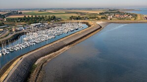 An aerial view of a marina with numerous boats docked along a curved shoreline, surrounded by residential buildings and open fields. - Apartment in Colijnsplaat near Lake and Sauna (Colijnsplaat)