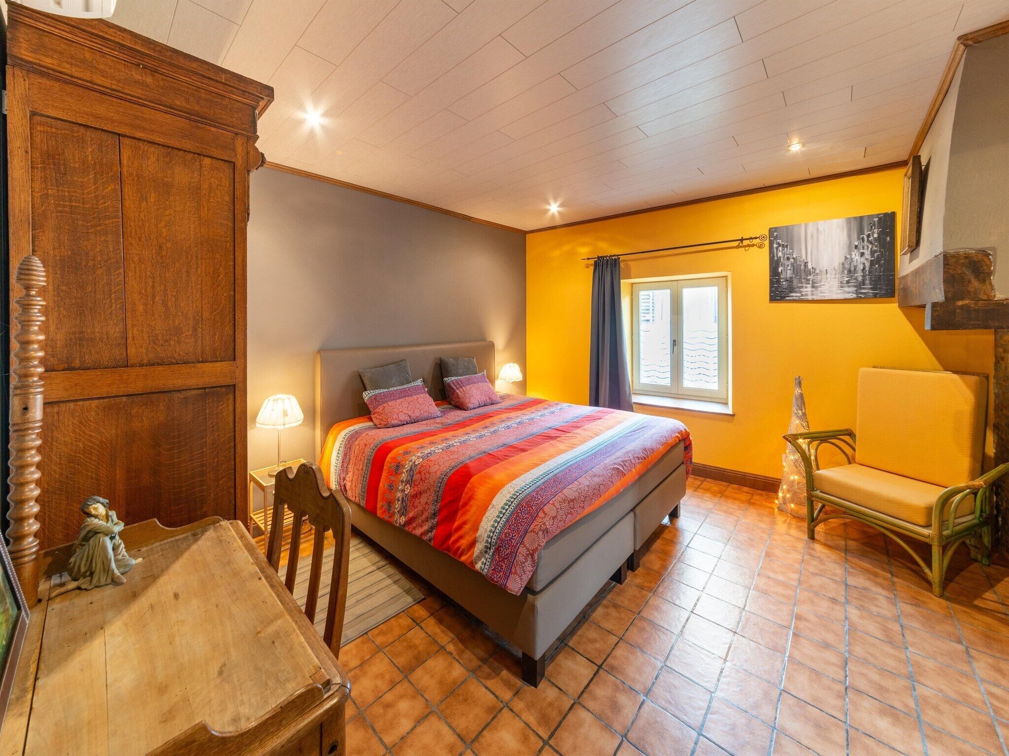 A bedroom with a bed, a chair, a wooden cabinet, and a window with curtains.