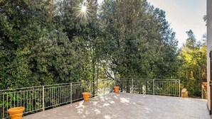 Eine gepflasterte Terrasse mit Metallgeländer, umgeben von dichtem Grün und Bäumen.