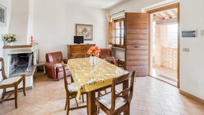 Una zona de menjador amb taula preparada per a quatre persones, una llar de foc, un televisor i un armari de fusta.
