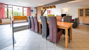 A modern dining area with a long wooden table and multiple chairs, a staircase, and a view of greenery outside. - Spacious Group Getaway with Garden (Ulestraten)