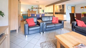 A modern living room with a sofa and armchairs, a wooden coffee table, and a kitchen in the background. - Spacious Group Getaway with Garden (Ulestraten)