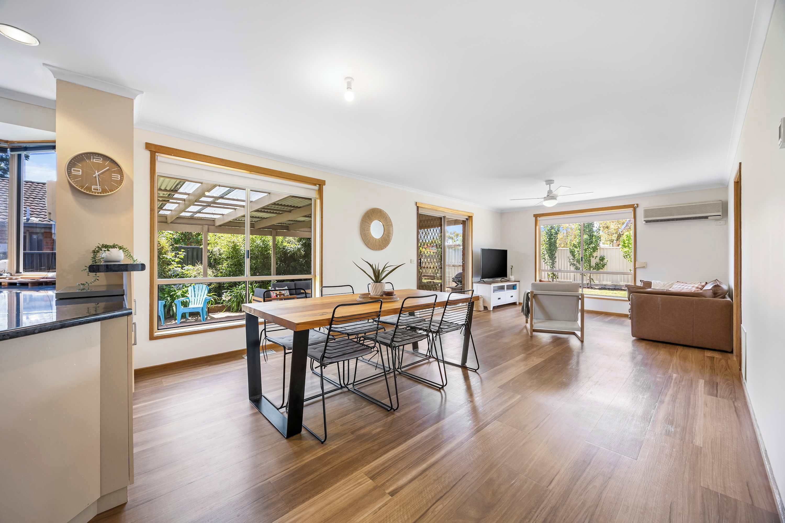 A modern kitchen with a dining area, large windows, and a flat-screen TV.
