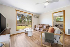 A modern living room with a sofa, a TV, a dining table, and a large window.