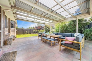 A covered patio with a wooden table and benches, a sofa, and a view of the backyard. - Tasteful 3BR On Towong, Alfredton (Alfredton)