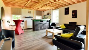 Una sala moderna con techo de madera, un sofá de cuero negro, una mesa roja y una cocina al fondo.
