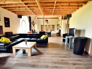 Un salon spacieux avec un plafond en bois, un canapé en cuir noir, une table basse en bois et un téléviseur.
