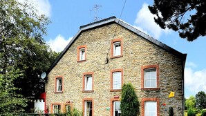 Un edificio de piedra con múltiples ventanas y una puerta, rodeado de follaje.