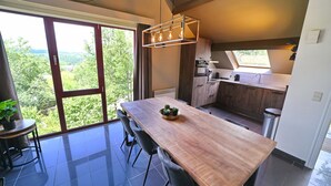 Une cuisine moderne dotée d’une grande fenêtre, un coin repas avec une table et des chaises en bois, et une vue sur l’extérieur.