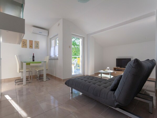 A modern living room with a grey sofa, a dining table with chairs, a TV, and a balcony with a view of greenery. - Apartment in Sveti Vid near the Adriatic (Malinska)