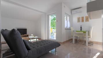 A modern living room with a sofa, a dining table with chairs, a TV, and a balcony with a view.