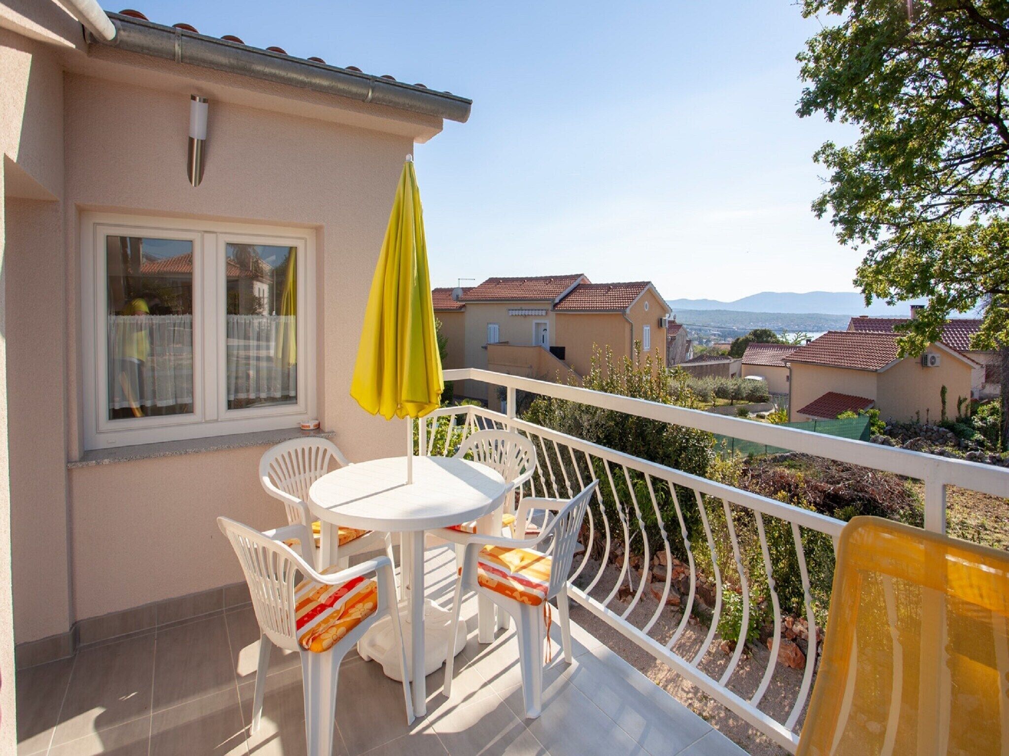 A balcony with a table and chairs, a yellow umbrella, and a view of neighboring houses.