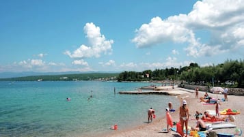 A beach with clear turquoise water, people swimming, and beachgoers relaxing.