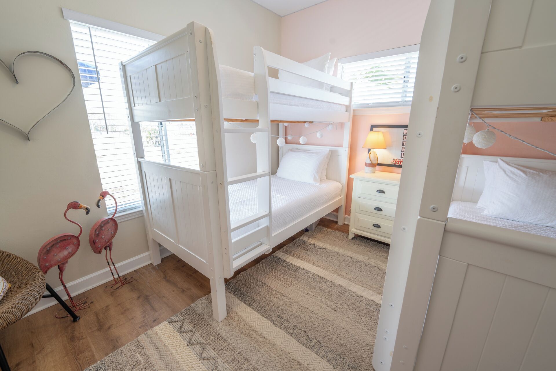 A room with bunk beds, a bedside table with a lamp, a small rug, and a wall decoration.