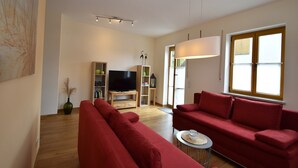 Una sala moderna con un sofá rojo grande, un televisor sobre un mueble de madera y un ventanal con persianas.