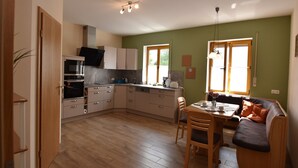Una cocina compacta con electrodomésticos modernos, un comedor con mesa y sillas de madera, y un sofá con cojines.