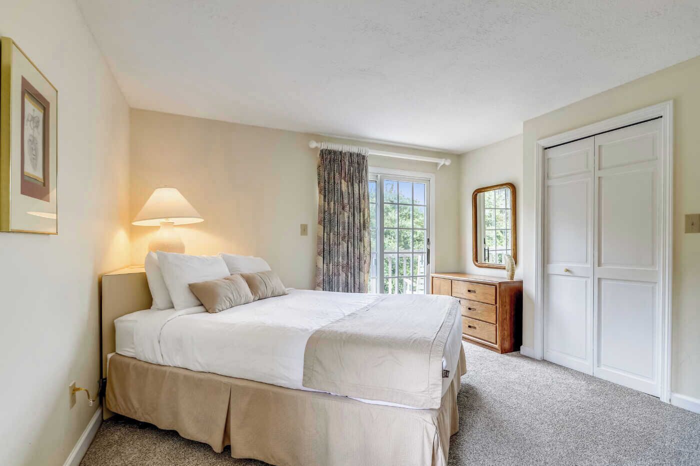A bedroom with a bed, bedside lamp, dresser, mirror, and a door.