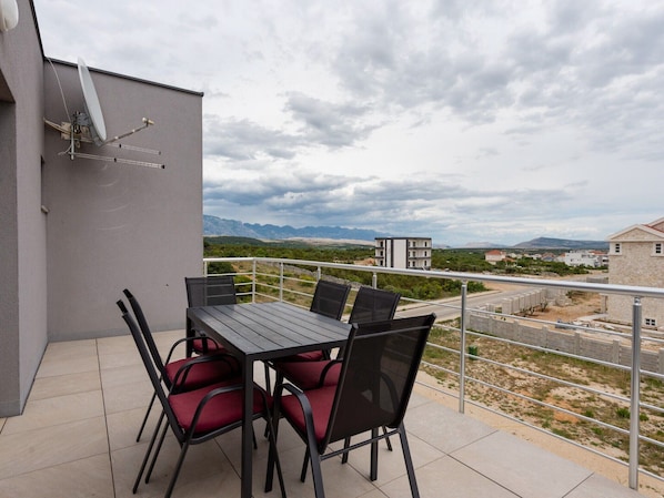 A balcony with a table and chairs, a satellite dish, and a view of a mountainous landscape.