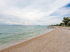 Una playa con orilla pedregosa, un muelle de madera y una línea costera distante.