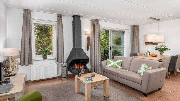 A modern living room with a fireplace, a sofa, a coffee table, and a dining area with a table and chairs. - Restyled house with fireplace, surrounded by green (Hoogersmilde)
