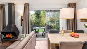 A modern living room with a fireplace, a dining area with a table set for two, and a view of the garden through large glass doors. - Restyled house with fireplace, surrounded by green (Hoogersmilde)
